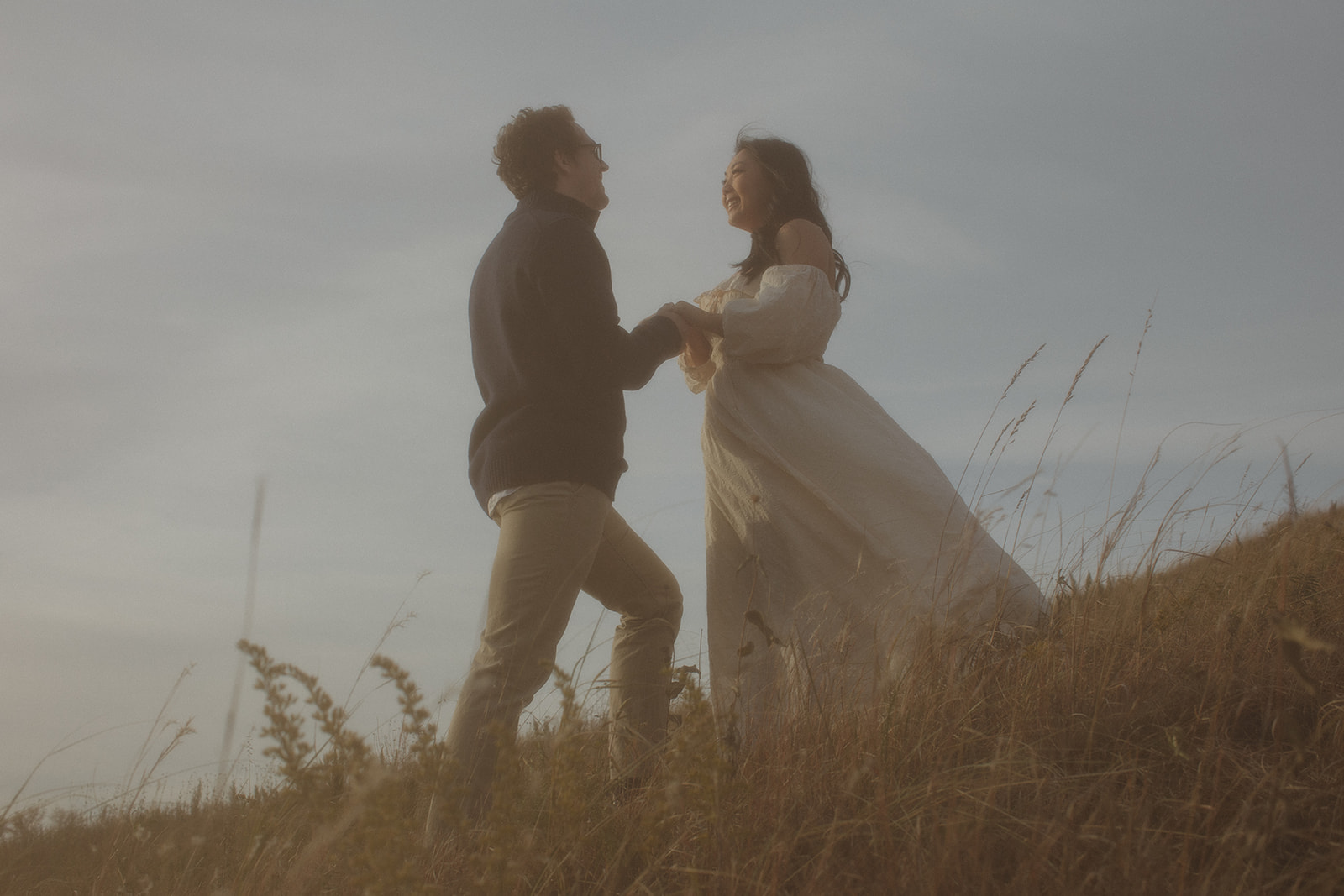 Couple stand on hill with sky behind them in a hazy photo.