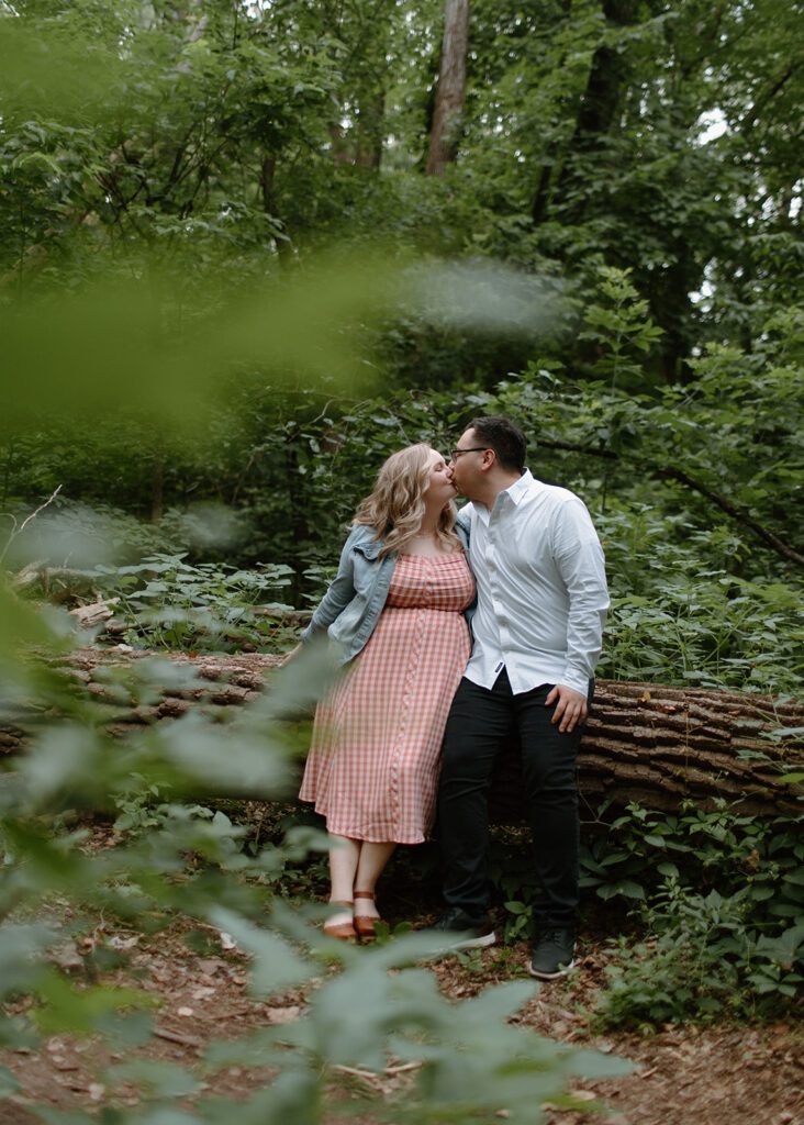 Couple cuddles by the river at neighborhood engagement session.