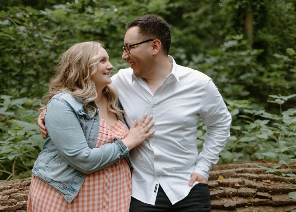 Couple cuddles by the river at neighborhood engagement session.